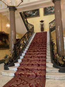 The grand marble staircase with gilded balustrade and burgundy carpet. 